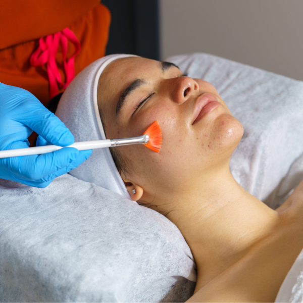 Beautician wearing blue gloves applying chemical peel on a young woman's face with a brush, during a cosmetic procedure Beautician wearing blue gloves applying chemical peel on a young woman's face with a brush, during a cosmetic procedure